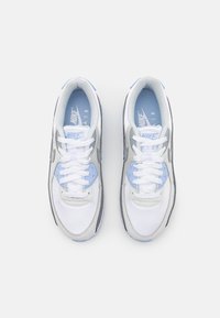 White and gray Nike sneakers with blue accents, featuring a textured design, round laces, and a cushioned sole. Logo visible on tongue.