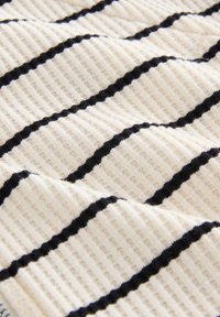 Textuurstof in crèmekleur met horizontale zwarte strepen. Het patroon heeft een geribbelde weefstructuur, met afwisselend gladde en verhoogde delen.