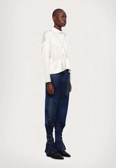 Vit satinblus med långa ärmar, rynkor och peplum, kombinerad med mörkblå denimbyxor med knappdetaljer vid ärmsluten och avslappnad passform.