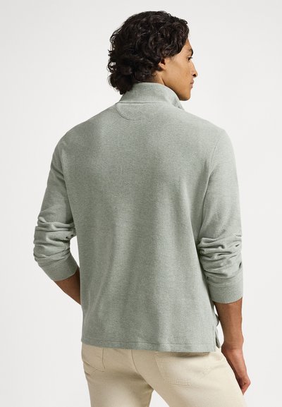 Light green pullover in a textured fabric, featuring a high collar and rolled-up sleeves. Designed with a relaxed fit and side slits.