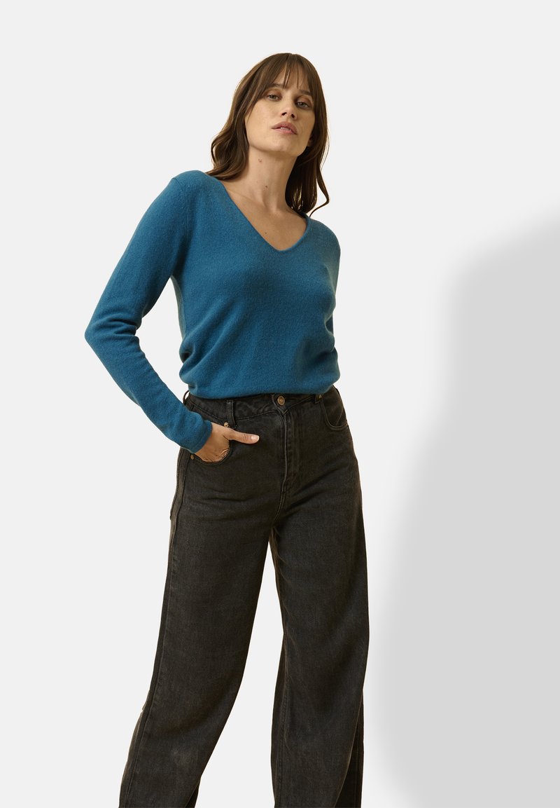 Suéter azul de cuello en V hecho de tela suave, combinado con unos pantalones vaqueros de pierna ancha negros y de cintura alta que tienen una parte delantera abotonada y bolsillos laterales.