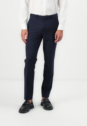 Mörkblå byxor i en mjuk väv, med en skräddarsydd passform, sidofickor och synliga bältesloopar, matchade med svarta loafers.