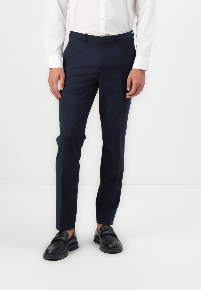 Pantaloni bleumarin dintr-un material neted, cu o croială ajustată, buzunare laterale și bucle vizibile pentru curea, asortați cu mocasini negri.