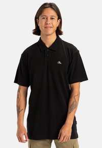 Polo shirt nera a maniche corte, con una pattina a tre bottoni e un piccolo logo bianco sul lato sinistro del petto. Tessuto liscio.