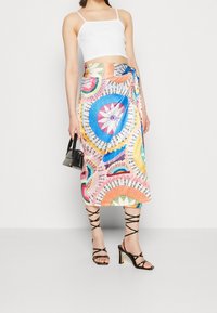 Jupe portefeuille multicolore avec des motifs circulaires en rose, bleu, jaune et blanc ; portée avec un crop top blanc et des talons noirs à lanières.