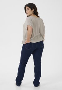 Blusa corta de manga corta en gris claro con pliegues, combinada con jeans azul oscuro. Los jeans tienen bolsillos traseros y un corte recto.