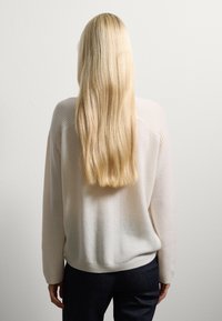 Maglione morbido e leggero color beige chiaro con dettagli a coste sulle spalle e un fit rilassato. Maniche lunghe e orlo arrotondato, indossato con jeans scuri.