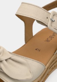 Μπεζ σουέτ σανδάλι με διακοσμητικό φιόγκο, ρυθμιζόμενο λουρί στον αστράγαλο και επενδυμένο, μαλακό τακούνι σε ανοιχτό καφέ χρώμα. Σόλα πλατφόρμας που μοιάζει με φελλό. Μέγεθος 4½.