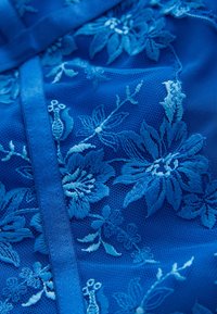 Mėlynas siuvinėtas audinys su gėlių raštais, sudėtinga detalizacija, tinklelio tekstūra ir kontrastinga satino apdaila.