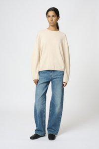 Beige oversize tröja med långa ärmar, tillsammans med ljusblå vida jeans. Skorna är svarta med en slät yta.