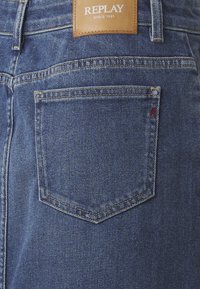 Jean en denim avec un bleu délavé classique, dotés d'une seule poche arrière et d'une étiquette en cuir emboutie avec "REPLAY SINCE 1981".