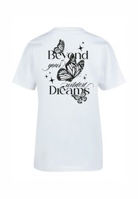 White cotton t-shirt featuring black graphic print of butterflies and the text "Beyond your wildest Dreams" on the back. Short sleeves.