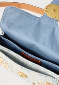 Τσαντάκι από ανοιχτό μπλε τζιν με χρυσά καρφιά, ανοικτό για να φαίνεται το εσωτερικό από ύφασμα ανοιχτού μπλε και καφέ δερμάτινο λουράκι με χρυσό κούμπωμα.