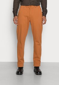 Calças em laranja enferrujado, feitas de mistura de algodão. Design de perna reta, com passantes para cinto e bolsos laterais. Botas de tornozelo pretas completam o look.