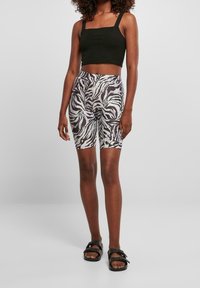 Zwarte crop top met dikke bandjes, gecombineerd met hoge shorts met een zwart-wit zebra patroon. Het model draagt zwarte sandalen.