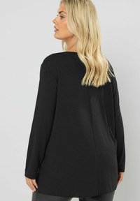 Maglia nera a maniche lunghe realizzata in tessuto morbido, con una vestibilità comoda, una leggera lucentezza e un orlo posteriore allungato per una maggiore copertura.