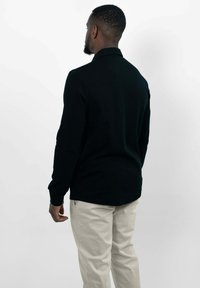 Schwarzes Langarm-Polohemd mit Kragen, kombiniert mit beigen Hosen. Das Hemd hat eine glatte Textur und eine gerade Passform.