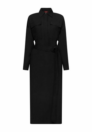 Personne portant une veste en polaire verte, une robe noire, un pull rayé noué à la taille, des bottes matelassées beiges, tenant un sac à cordon jaune Esprit.