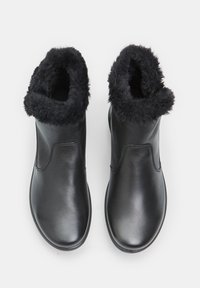 Botas de tobillo de cuero negro con un puño de piel de pelo negro esponjoso, superficie suave, punta redondeada y detalles de costura lateral. Adecuadas para el uso en climas fríos.