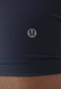 Mörkblå stretchiga sportshorts i tyg med en mjuk yta, som har en diskret logotyp och kontrasterande sömnad längs nederkanten.