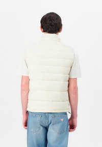 Leichte Steppweste mit wattierten Abschnitten, hohem Kragen und subtiler Satin-Optik, kombiniert mit hellblauen Jeans.