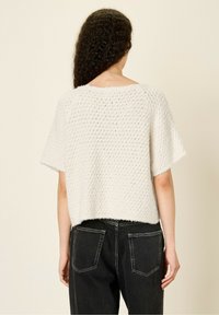 Pull blanc en texture avec des manches courtes et une coupe décontractée. Il a un col arrondi et un dos court, associé à un jean en denim noir.