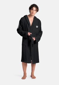 Sort badehætte i terrycloth med hætte, lange ærmer, forlommer og bindebånd i taljen. Har logo på brystet og stribede accenter på ærmerne.