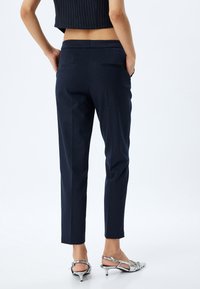 Marineblaue, taillierte Hose mit schmalem Schnitt, ausgestattet mit zwei Gesäßtaschen und einer glatten Textur, kombiniert mit silberfarbenen, hohen Sandalen.