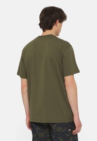 Olivgrön bomulls t-shirt med avslappnad passform, korta ärmar och rundad halsringning, visad bakifrån, kombinerad med mönstrade shorts.