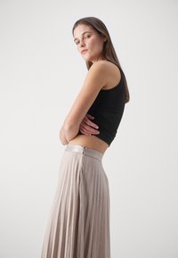 Top negro ajustado combinado con una falda plisada beige que tiene una cinturilla metálica y una cremallera discreta en la parte posterior.