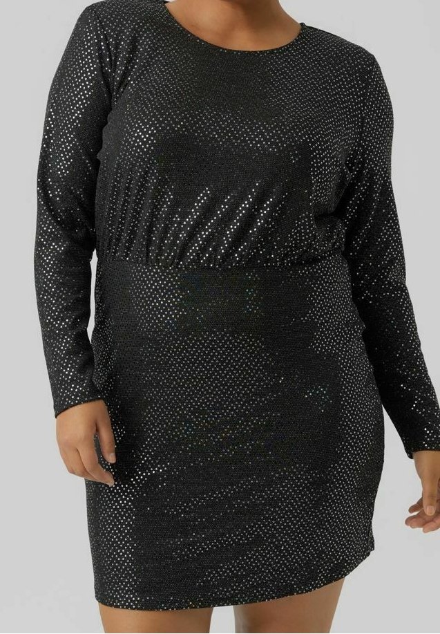 Femme portant une robe noire ajustée à manches longues avec des points en sequins argentés et un col rond, debout devant un fond uni.