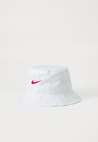 Chapeau seau blanc avec un petit logo rouge Nike à l'avant. Fabriqué en tissu léger avec un large bord incliné vers le bas.