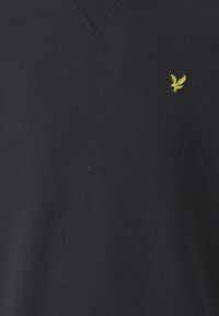Černá mikina s výstřihem do V vyrobená z měkkého materiálu, na hrudi s malým žlutým vyšitým logem ptáka. Minimalistický design, bez vzorů.