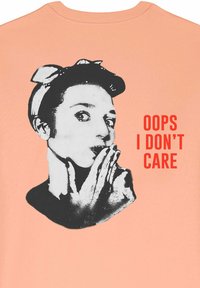 T-shirt pêche avec un graphique en noir et blanc représentant une personne avec un bandeau, les mains sur la bouche, et une impression rouge indiquant "OUPS, JE M'EN FICHE."