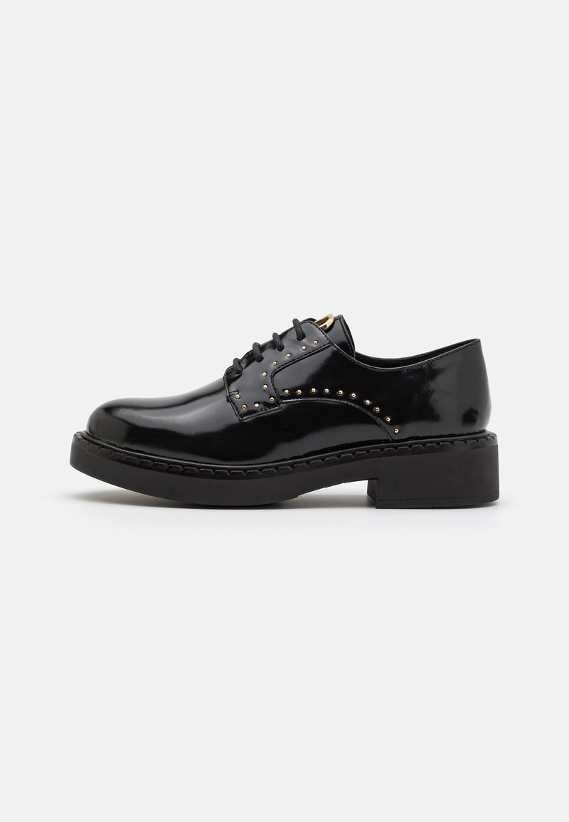 Chaussure à lacets en cuir verni noir avec semelle épaisse et petits clous dorés le long du côté et des œillets, sur un fond clair.