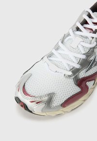 White mesh sneaker with silver and burgundy accents, featuring a textured surface, lace-up design, and a black outsole.