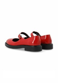 Zapatos Mary Jane de charol rojo con punta redonda, tira en el tobillo y suela de goma negra. Cuenta con una hebilla y un acabado suave.