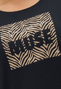 Sort t-shirt med zebra-stribemønster og teksten "Vær din egen MUSE" i fede, store bogstaver. Glat tekstur.