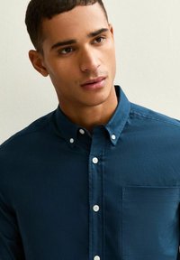 Overhemd met knopen in donkerblauwe stof. Heeft een borstzak, witte knopen en een kraag. Gladde textuur met een slim-fit ontwerp.
