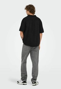 Sort kortærmet skjorte lavet af et tekstureret stof, parret med grå jeans. Modellen står i profil og fremviser en afslappet pasform og kravedesign.