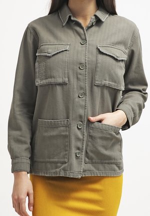 Olijfgroene button-up jas van katoen, met twee borstzakken, twee onderste zakken en ruwe randdetails op de zakflappen.