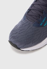 Baskets avec un dessus en mesh texturé gris foncé, arborant des accents bleus. Semelle en caoutchouc avec un capuchon noir pour les orteils et un design à lacets.