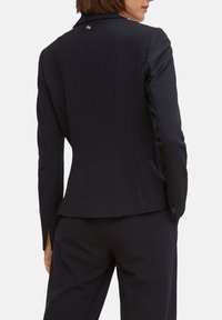Blazer blu navy con vestibilità sartoriale, caratterizzato da uno spacco doppio, tessuto testurizzato e un logo sul retro. Adatto per abbigliamento formale.