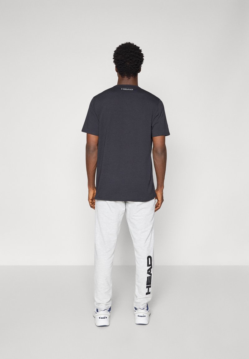 Camiseta de algodón negra y pantalones de chándal grises. La camiseta tiene mangas cortas y un detalle de logo en la parte posterior; los pantalones de chándal presentan un gran logo impreso en el costado.