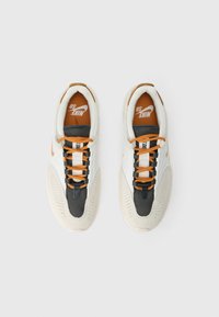 Balts, melns un oranžs Nike SB apavu pāris ar oranžām auklītēm, skatoties no augšas uz gaiši pelēka fona.