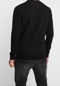 Zwarte sweatshirt met lange mouwen, geribbelde manchetten en een ronde hals. Gemaakt van een zachte, gestructureerde stof. Heeft een eenvoudig, effen ontwerp.