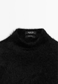 Maglione a collo alto in cashmere nero con una texture morbida e pelosa. Le etichette all'interno indicano il marchio e la composizione dei materiali.