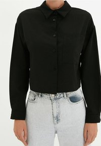 Czarna długosleeve koszula zapinana na guziki z kołnierzykiem i kieszonką na piersi, noszona wpuszczona w jasnoniebieskie dżinsy z wysokim stanem.