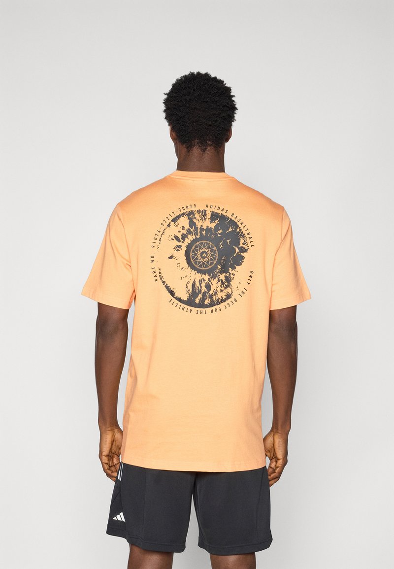 T-shirt en coton orange à manches courtes avec un design graphique circulaire noir et du texte au dos, avec un col rond et une coupe décontractée.