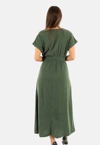 Vestido verde, de largo hasta la rodilla, hecho de tela ligera con mangas cortas y cintura ceñida. Presenta un corte recto y una textura sutil.